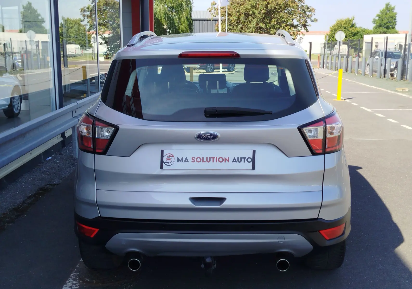 Vue arrière d'un Ford Kuga gris clair 2019 avec double sortie d'échappement et attelage visible sur parking.