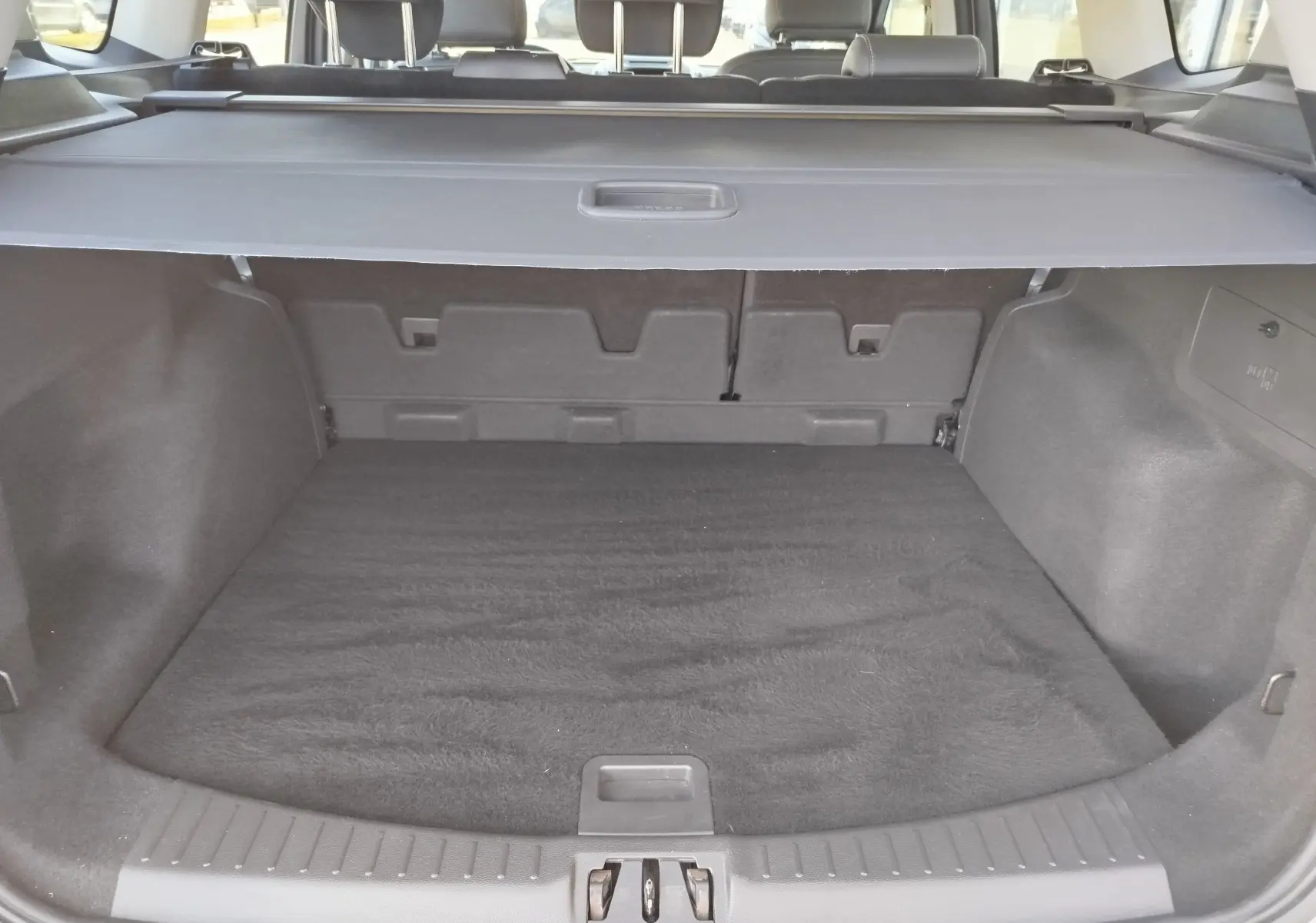 Coffre ouvert vu de l'arrière d'un Ford Kuga gris clair 2019, avec cache-bagages et intérieur noir.