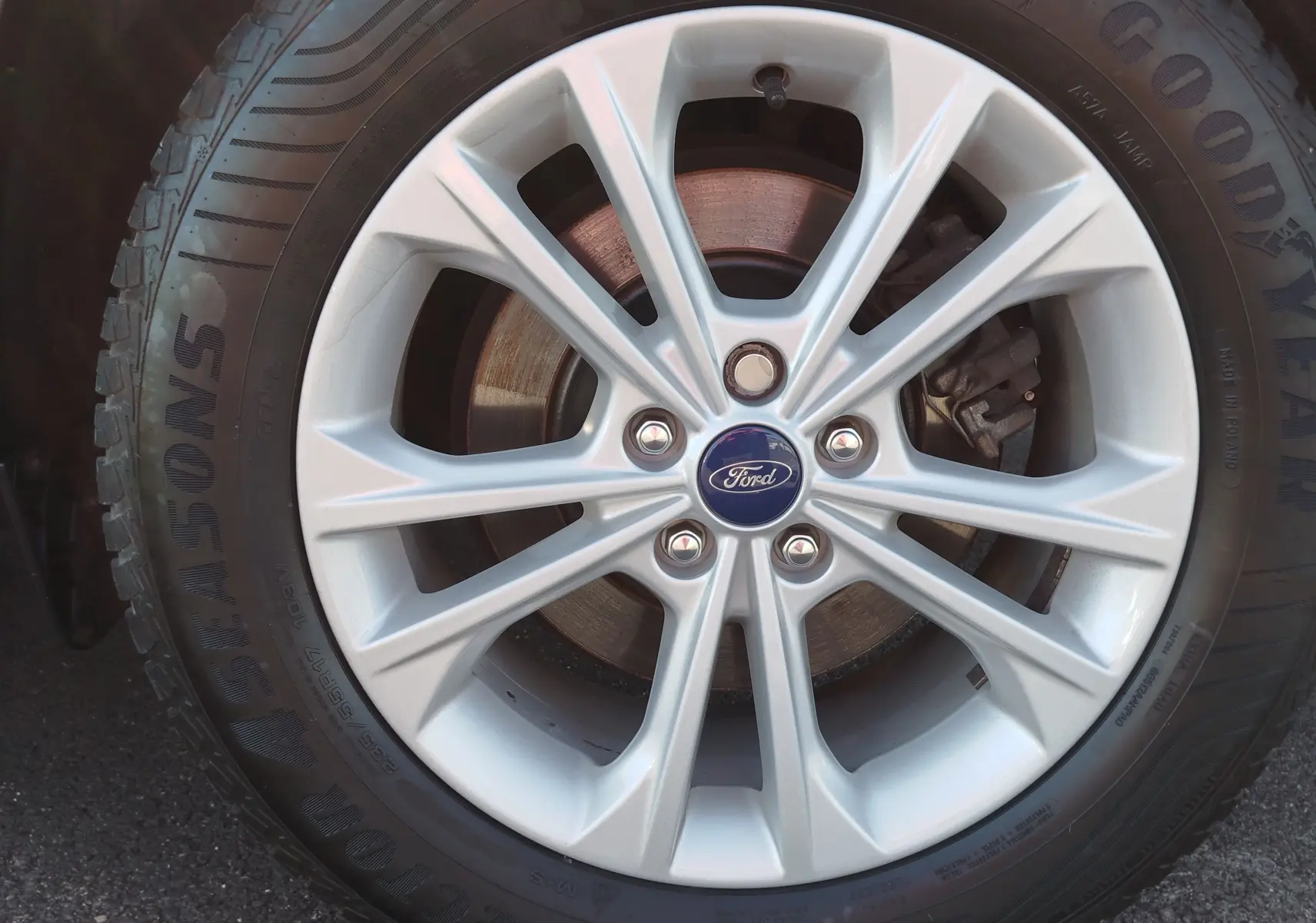 Gros plan sur la jante alliage argentée d'un Ford Kuga gris clair, avec logo Ford au centre et pneu Goodyear visible.