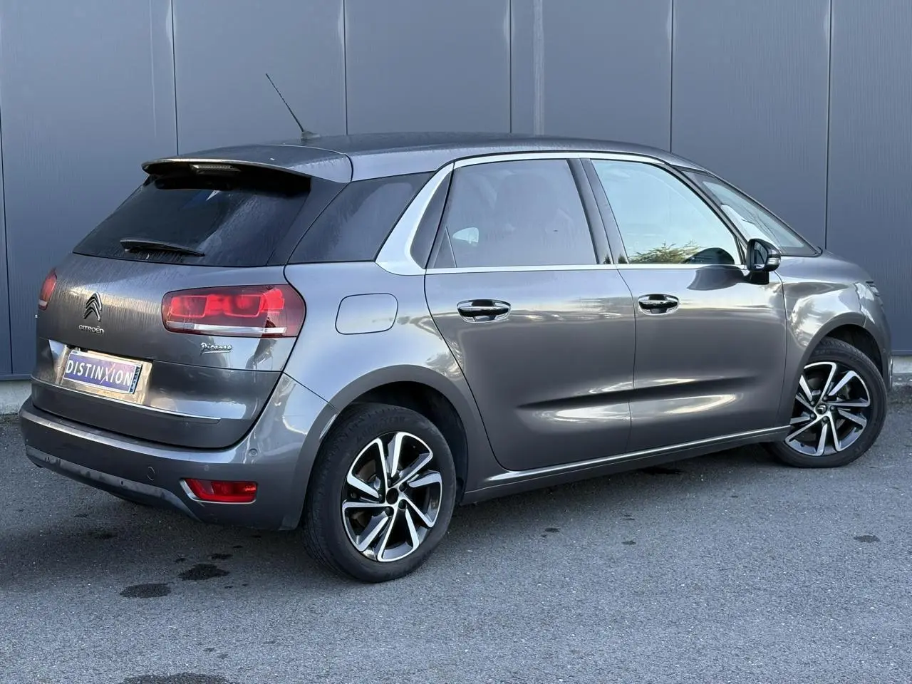 Vue 3/4 arrière côté droit d'une Citroën C4 Picasso gris Platinium avec jantes alliage bi-ton et hayon électrique.