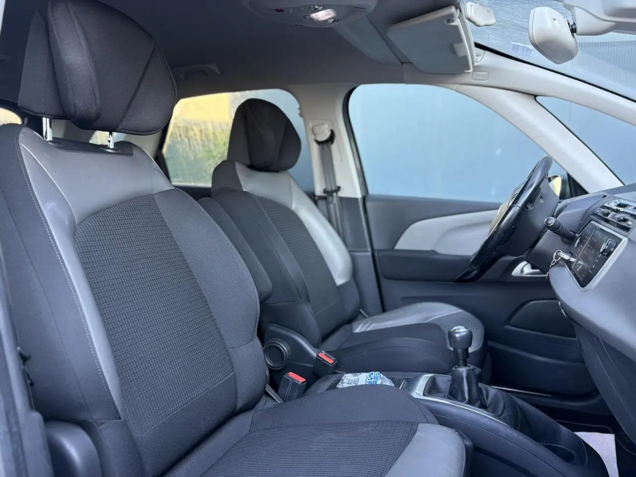 Vue intérieure côté conducteur de la Citroën C4 Picasso 2017, sièges tissu noir et cuir gris, volant cuir et levier de vitesses manuel.