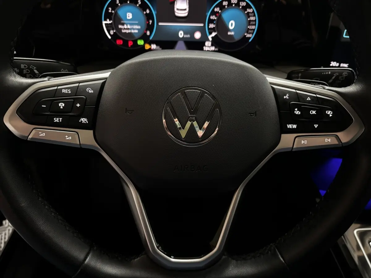 Vue rapprochée du volant cuir multifonctions d'une Volkswagen Golf 1.5 ETSI noire, avec tableau de bord digital lumineux.
