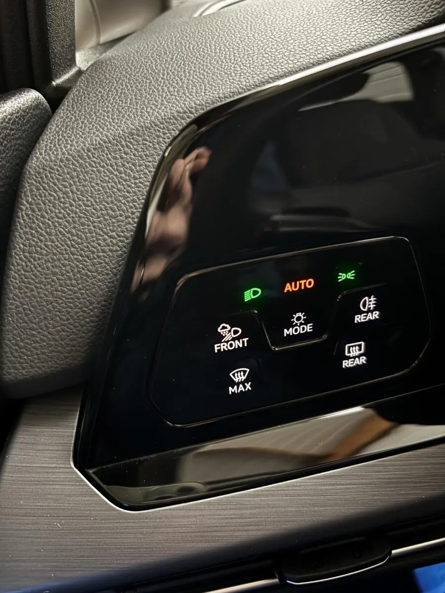 Gros plan sur le panneau de commandes d'éclairage noir brillant du Volkswagen Golf 2024, avec voyants verts et orange allumés.