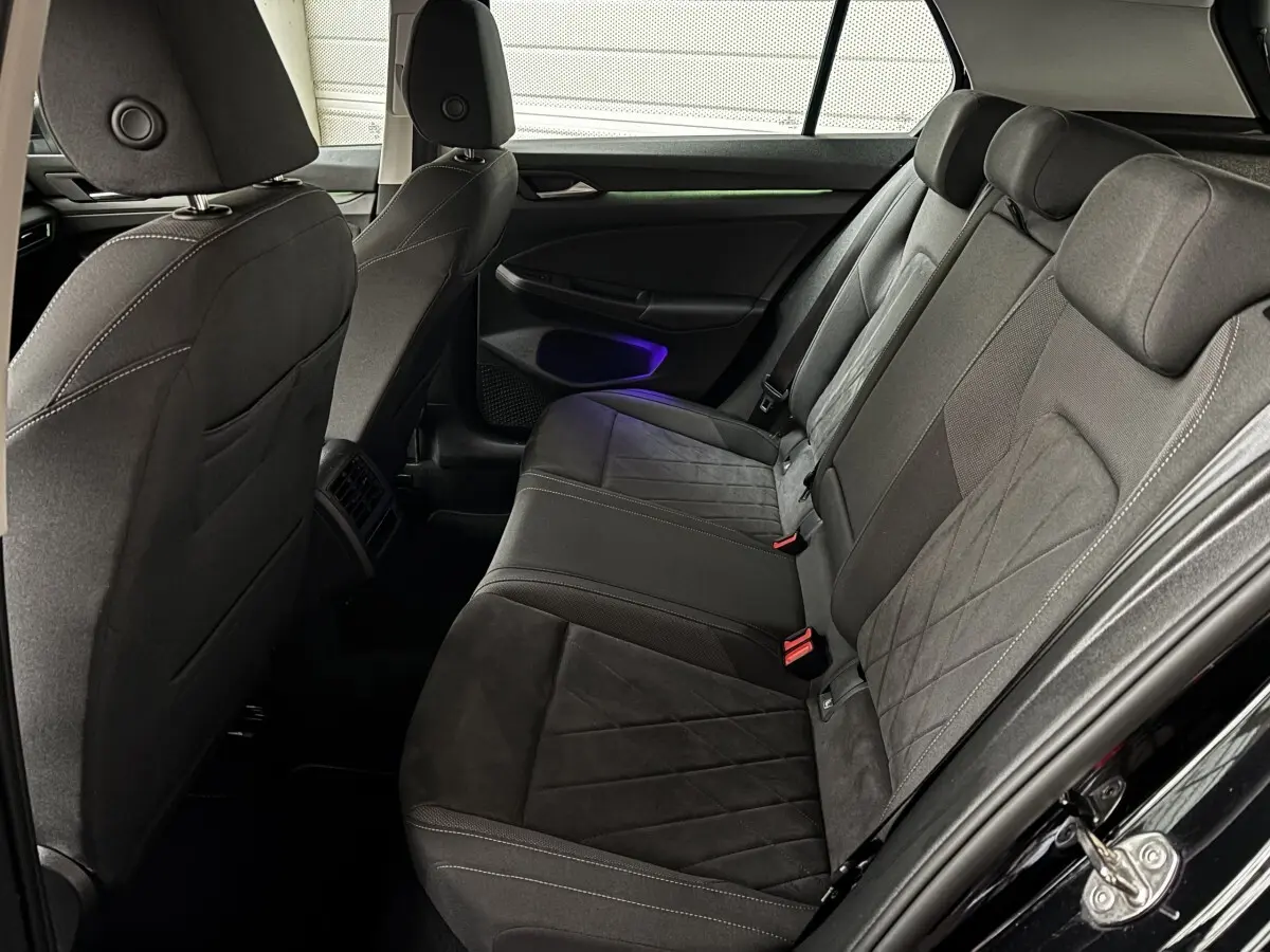 Vue latérale droite de l'arrière de la Volkswagen Golf noire 2024, montrant les sièges en tissu et alcantara avec éclairage d'ambiance violet.