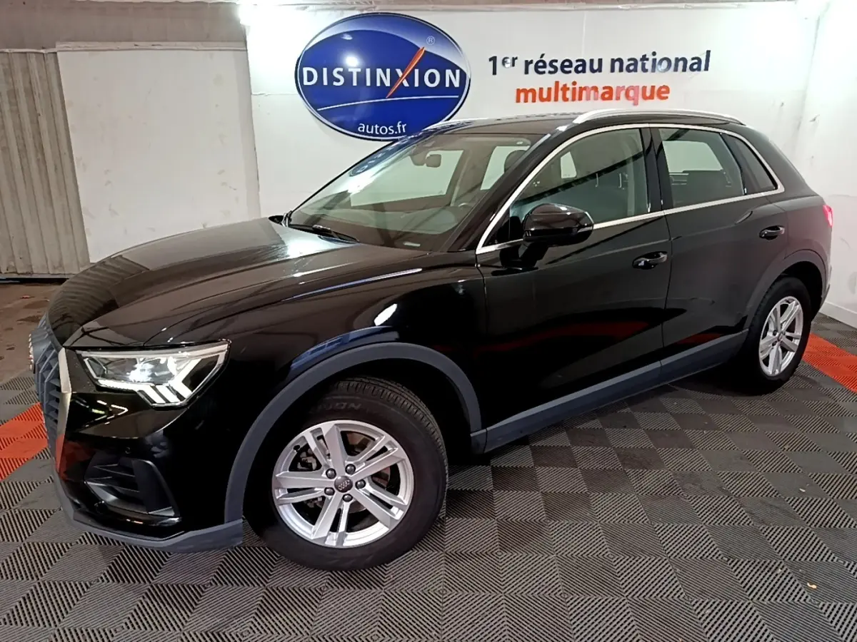 Audi Q3 noir vue 3/4 avant droit dans un showroom avec jantes argentées et phares allumés.