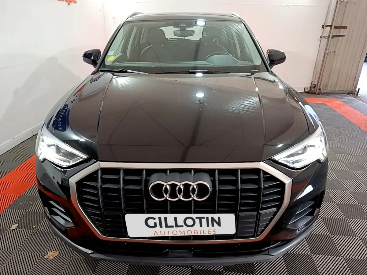 Vue avant d'un Audi Q3 noir 2020 avec calandre chromée et phares LED allumés dans un garage.