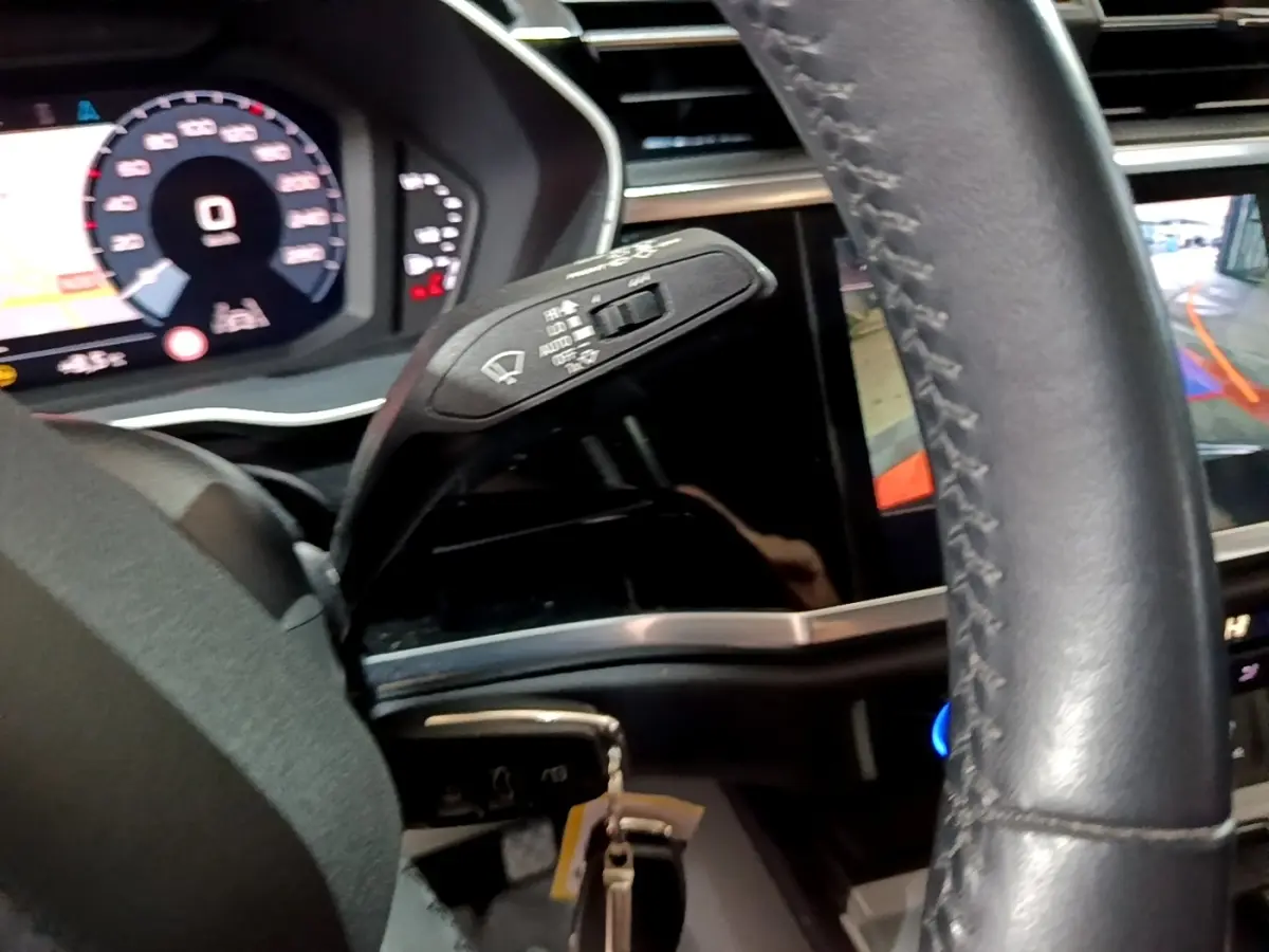 Vue intérieure rapprochée côté gauche du volant cuir d’un Audi Q3 35 TDI 150 S tronic avec tableau de bord numérique et caméra de recul.