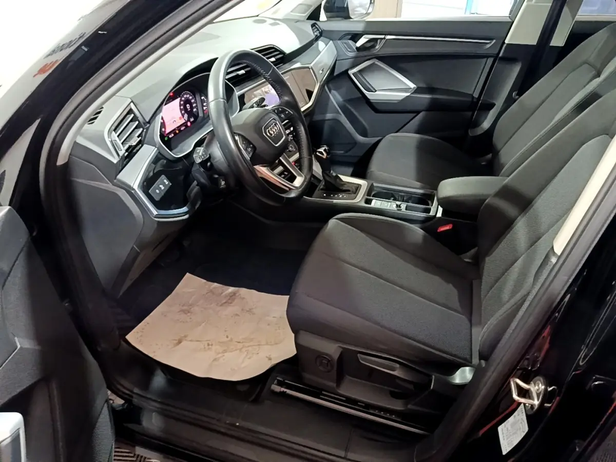 Intérieur côté conducteur de l’Audi Q3 noir 2020, montrant sièges tissu noirs et tableau de bord digital moderne.