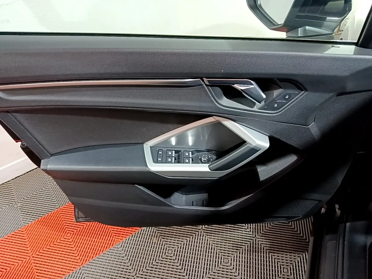 Vue rapprochée de la porte côté conducteur noire de l'Audi Q3 2020 avec commandes de vitres et rétroviseurs intégrées.