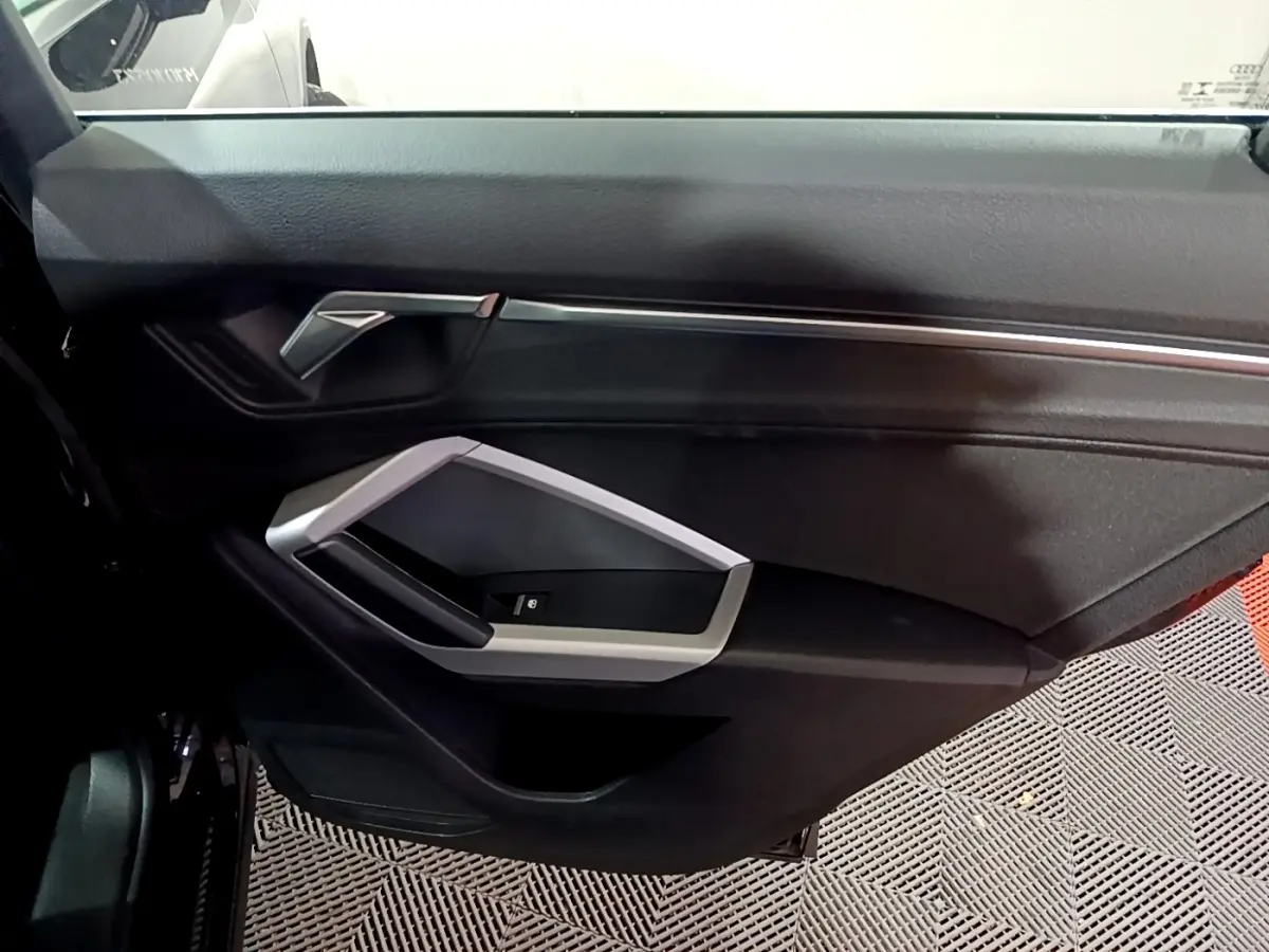 Vue intérieure du panneau de porte côté gauche noir de l'Audi Q3 35 TDI 150 S tronic Business Line avec poignée argentée.