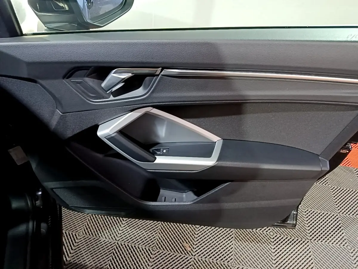 Détail de la porte côté gauche de l'Audi Q3 35 TDI 150 S Tronic Business Line noire avec poignée argentée et commandes de vitre.