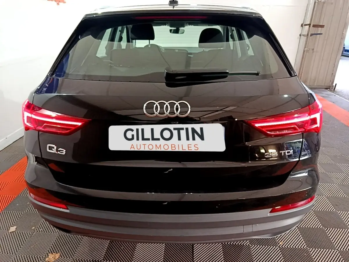 Vue arrière d'un Audi Q3 noir 35 TDI avec feux LED allumés et logo Audi visible sur un sol à damier.