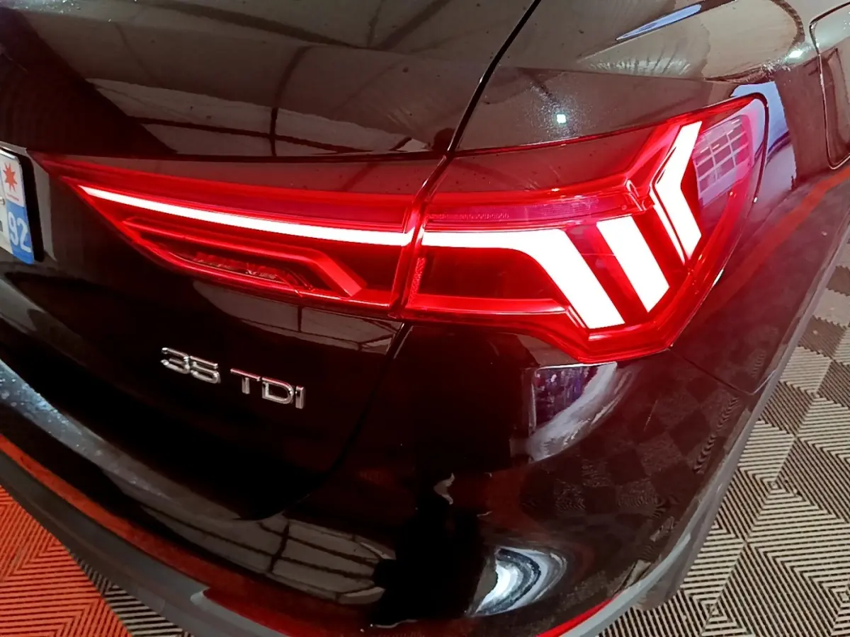 Gros plan sur le feu arrière droit rouge vif d’un Audi Q3 noir 35 TDI avec logo visible sur le coffre.