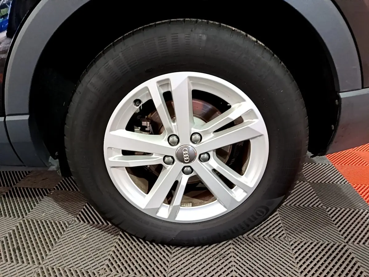 Gros plan sur la roue avant gauche avec jante argentée et logo Audi du SUV noir Audi Q3 35 TDI 2020.