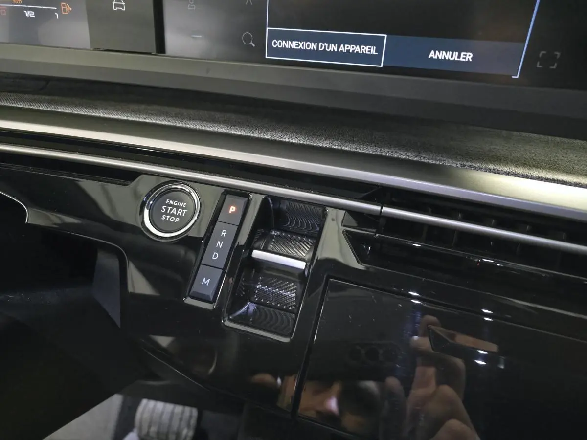 Gros plan sur la console centrale noire laquée du Peugeot 3008 gris hybride, avec bouton start/stop et sélecteur de boîte automatique.