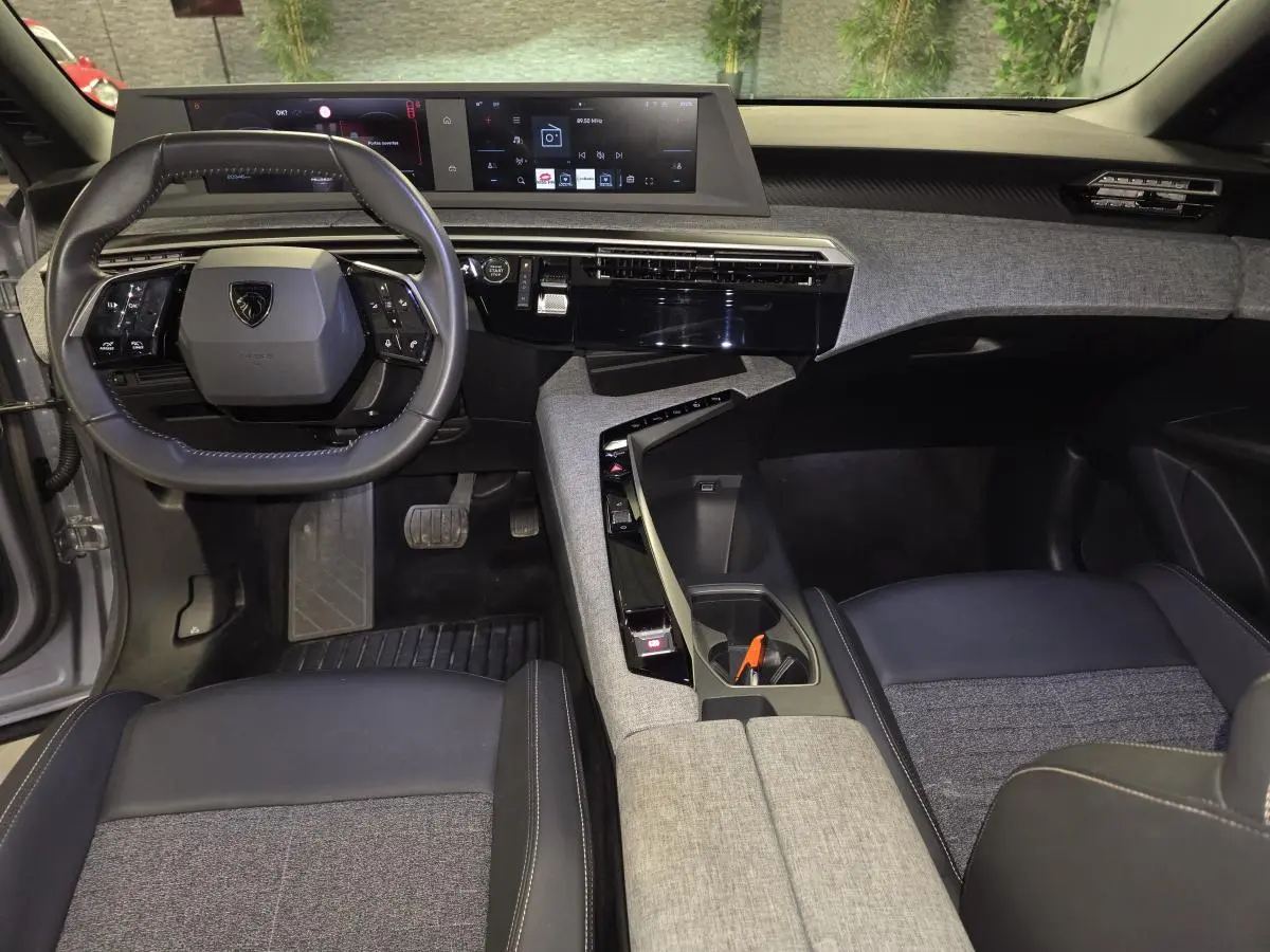 Vue intérieure du tableau de bord et volant Peugeot 3008 2025, avec sellerie tissu gris et console centrale design épuré.