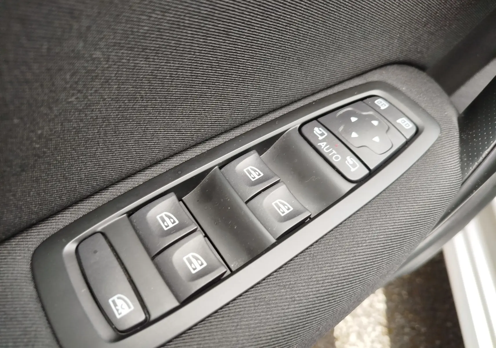 Gros plan sur les commandes de lève-vitres et réglage des rétroviseurs côté conducteur de la Renault Mégane gris Titanium 2018.