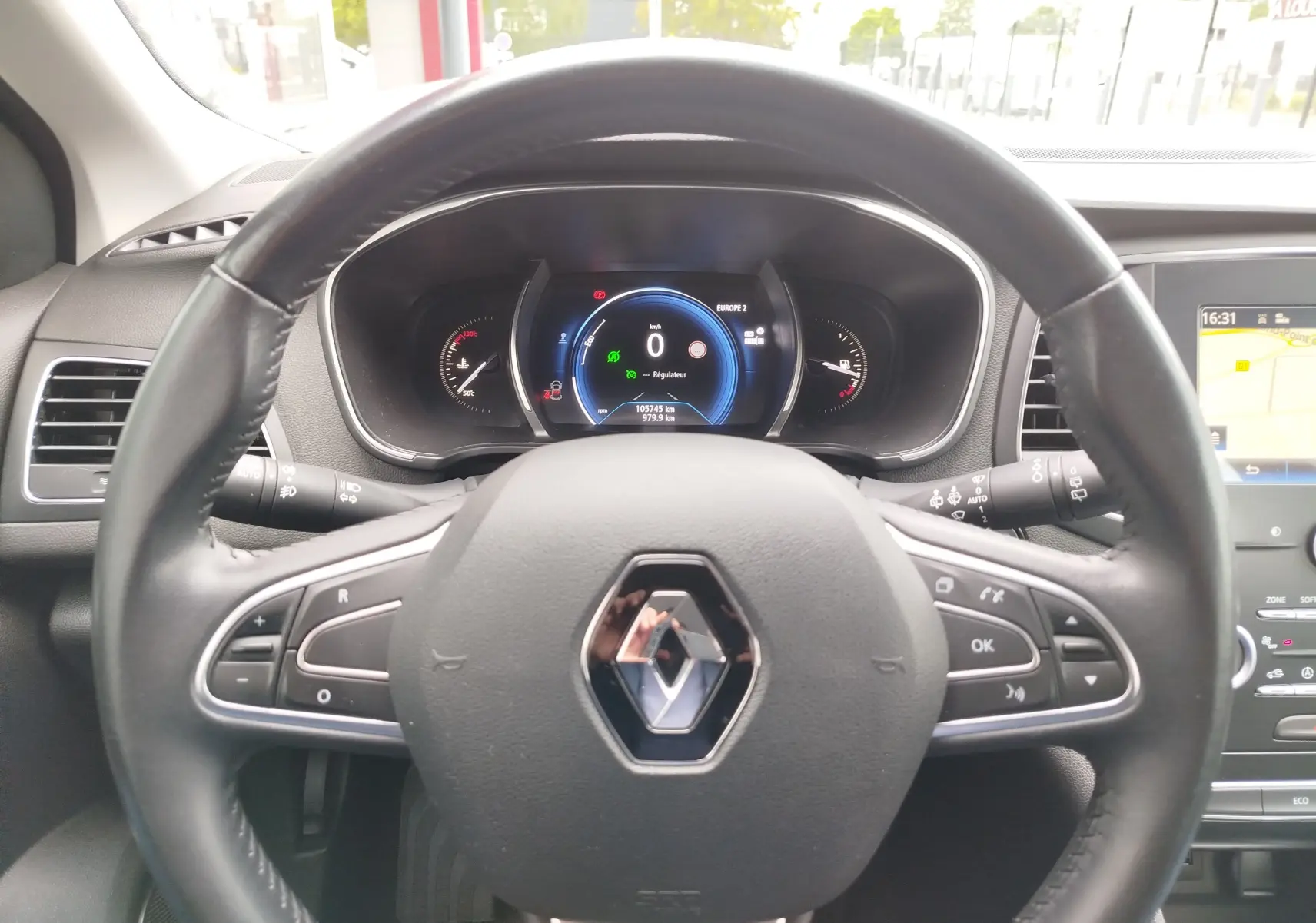 Vue intérieure centrée sur le volant Renault et le tableau de bord numérique de la Mégane gris titanium de 2018.
