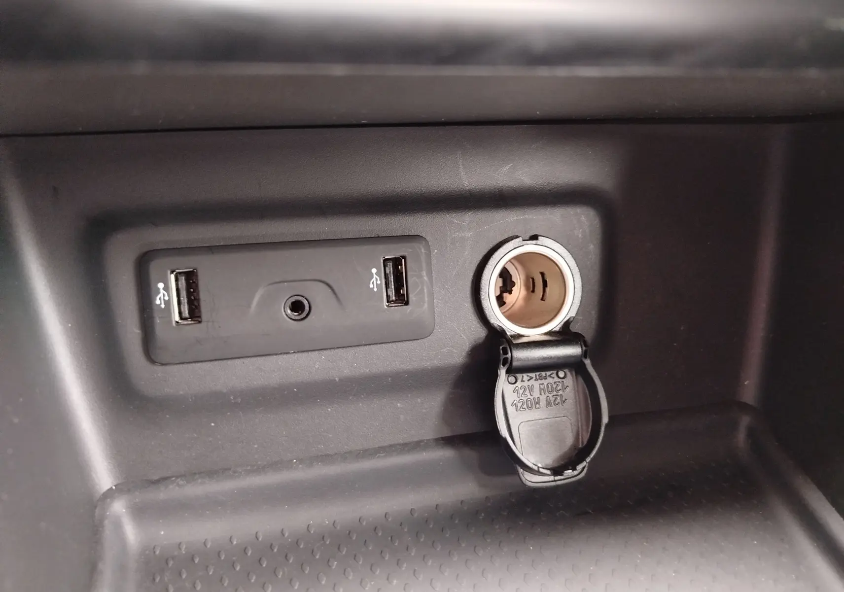 Gros plan sur la console centrale d’une Renault Mégane gris titanium 2018, montrant deux ports USB et une prise 12V ouverte.
