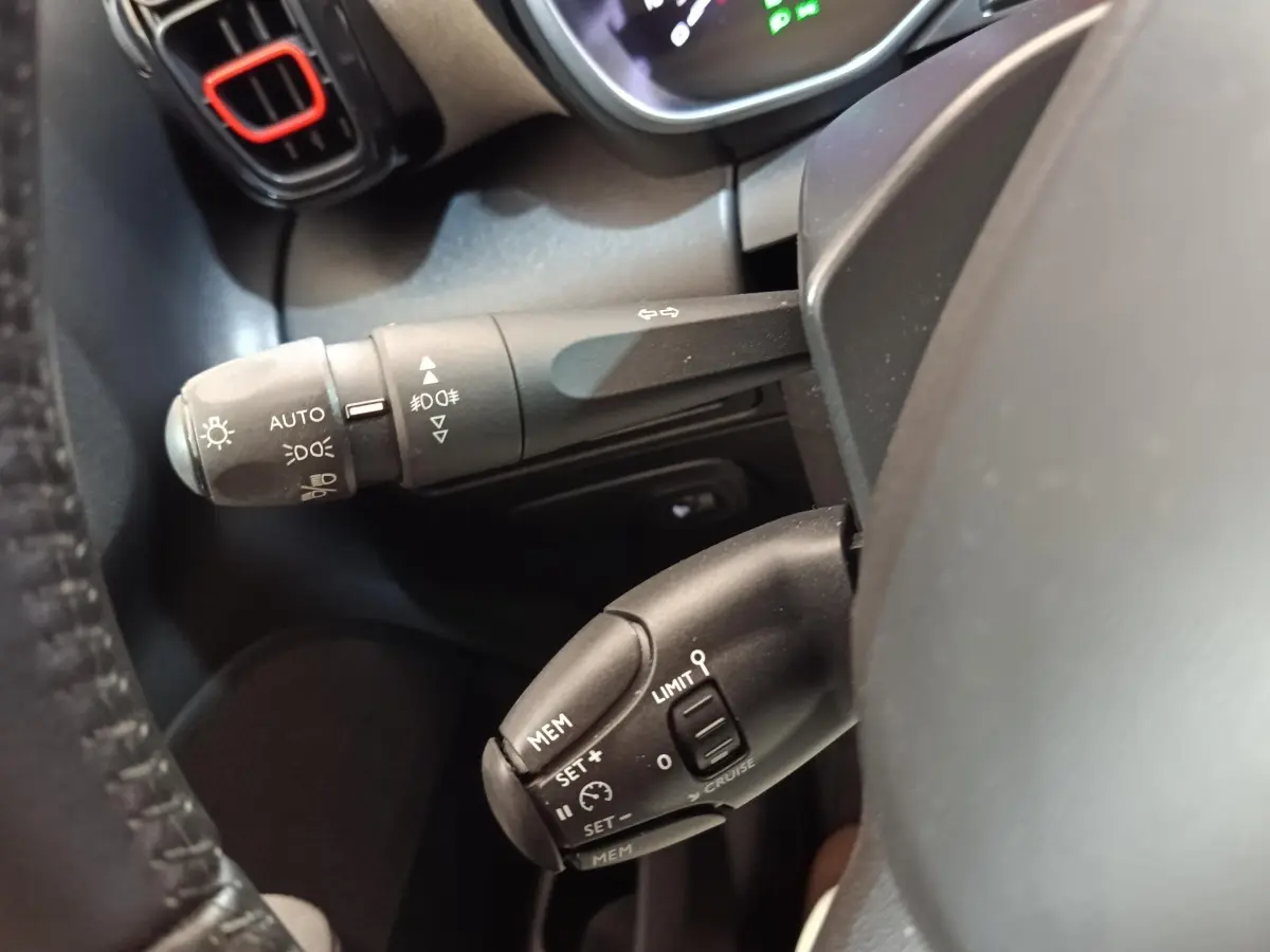 Gros plan sur les commandes au volant côté gauche du Citroën C3 Aircross beige, avec réglages feux et régulateur de vitesse.