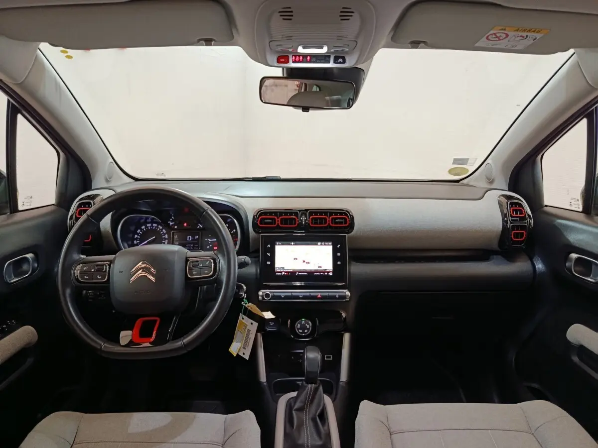 Vue intérieure frontale du tableau de bord de la Citroën C3 Aircross 2021, avec volant cuir noir et touches rouges sur aérateurs.