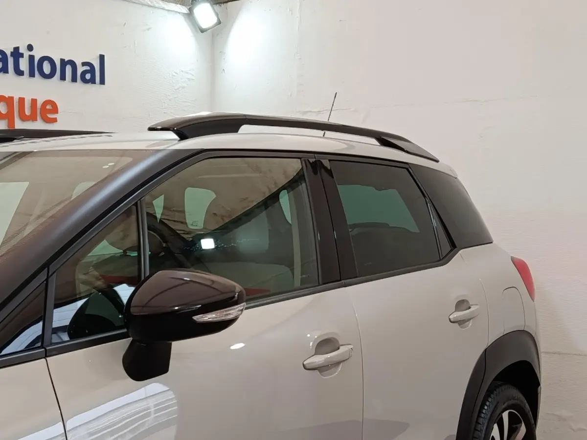 Vue latérale gauche d'un Citroën C3 Aircross beige avec toit et rétroviseur noir, dans un espace intérieur.