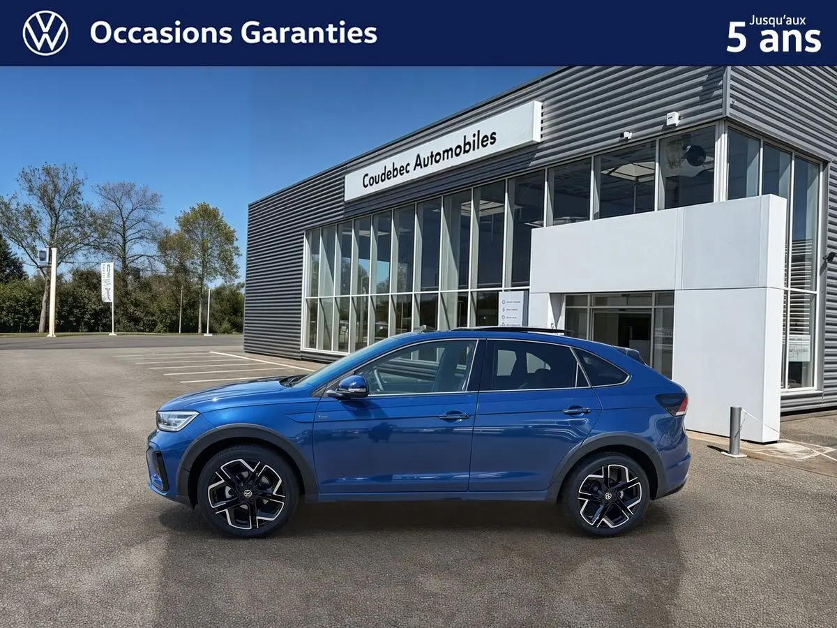 Profil côté gauche du Volkswagen Taigo bleu métallisé 2025, avec jantes alliage noires et toit ouvrant en verre.