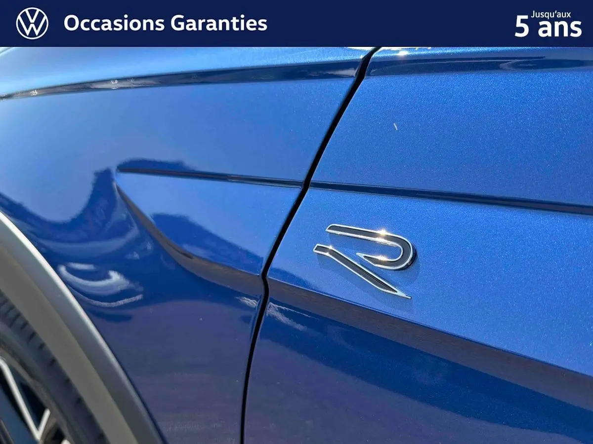 Détail du logo "R" sur l'aile avant droite d'un Volkswagen Taigo bleu métallisé sous lumière naturelle.