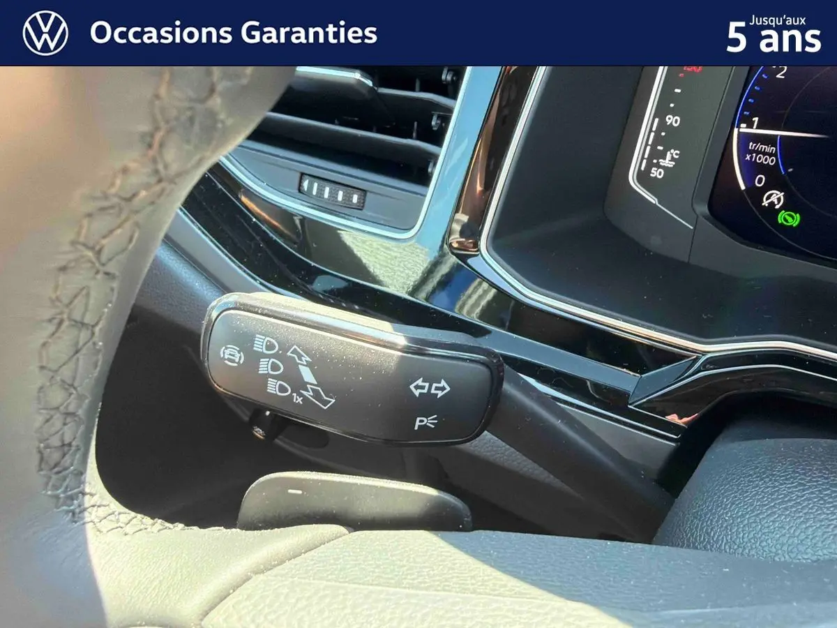 Gros plan sur la manette de clignotant à gauche du volant d’un Volkswagen Taigo bleu, tableau de bord digital visible.