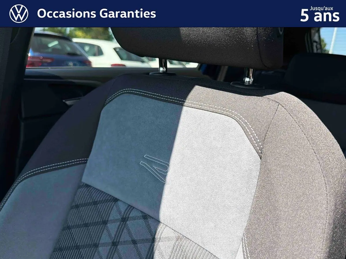 Détail du siège avant gris avec surpiqûres blanches et logo R embossé, intérieur du Volkswagen Taigo 2025.