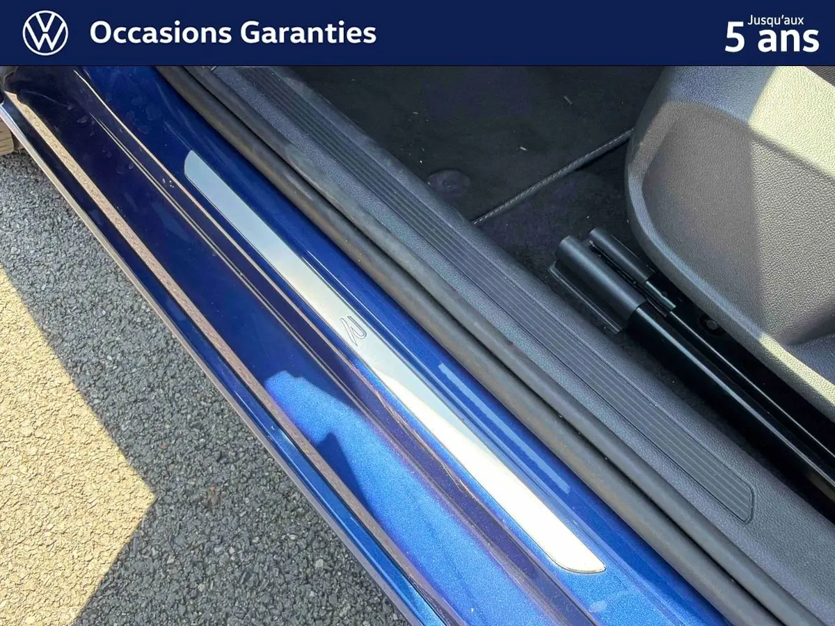 Gros plan sur la porte côté conducteur d'un Volkswagen Taigo bleu métallisé avec seuil de porte en aluminium.