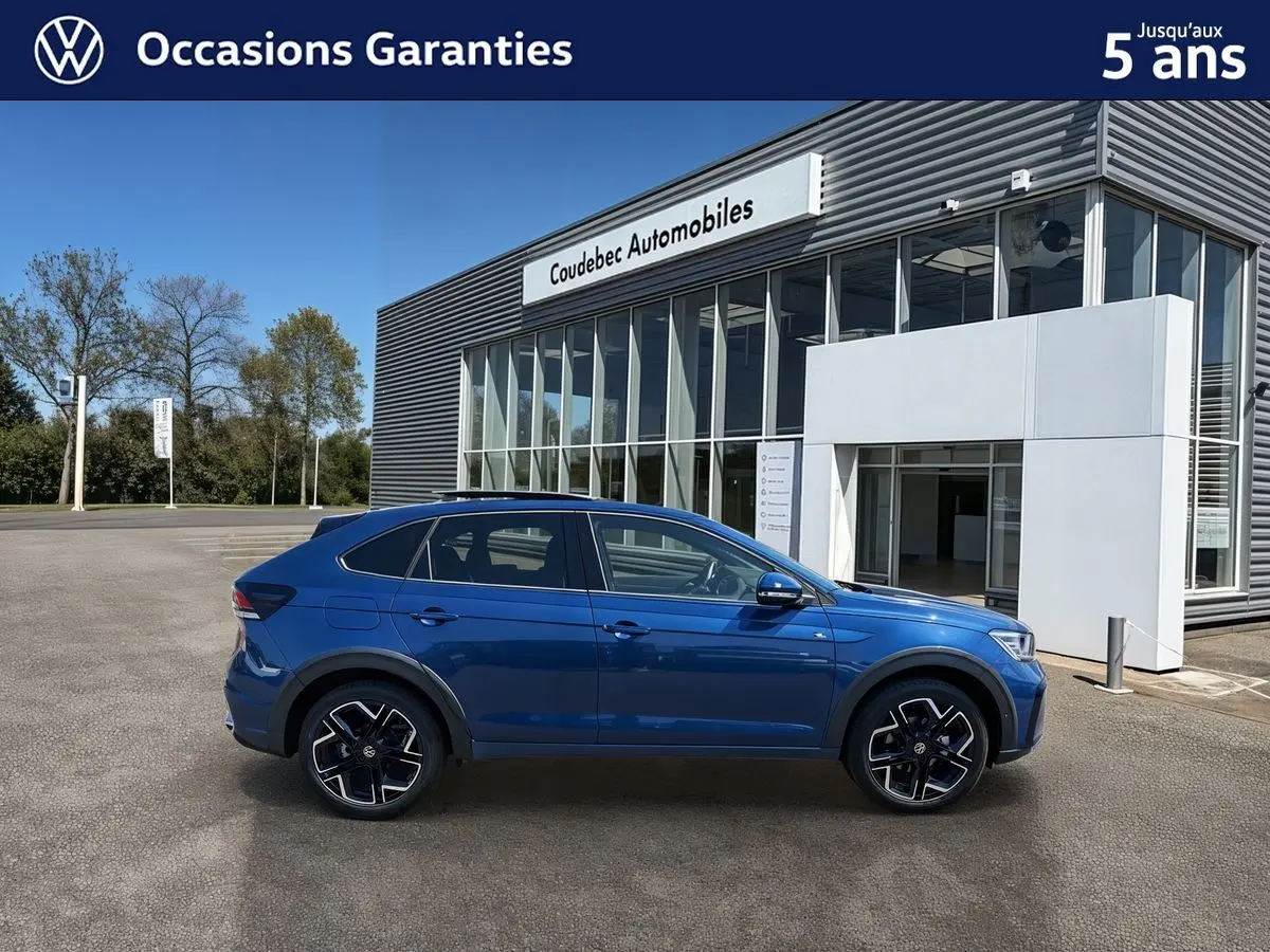 Profil côté gauche d'un Volkswagen Taigo bleu métallisé 2025 avec jantes alliage noires devant un bâtiment moderne.