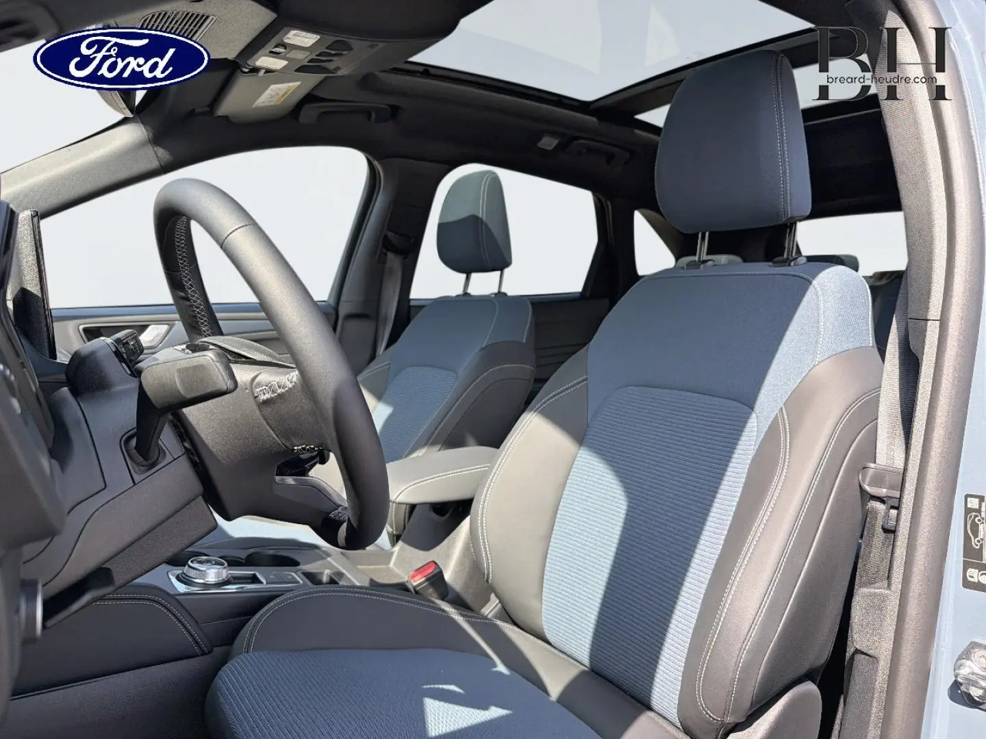 Vue intérieure côté conducteur du Ford Kuga 2026 bleu avec sièges bicolores et toit ouvrant panoramique.
