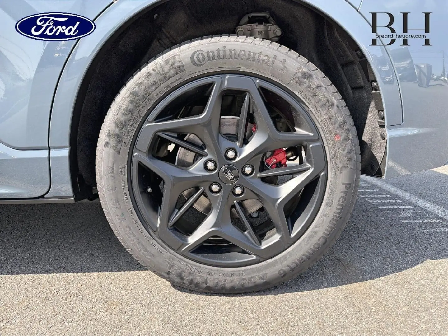 Gros plan sur la roue avant droite du Ford Kuga bleu, jante alliage noire avec étrier de frein rouge visible.