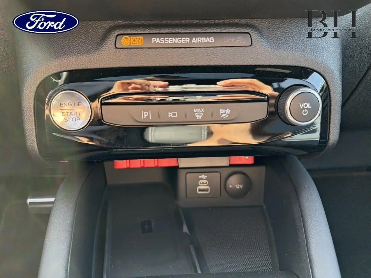 Détail de la console centrale du Ford Kuga 2026 avec bouton start/stop, commandes clim et prises USB/12V en vue frontale rapprochée.