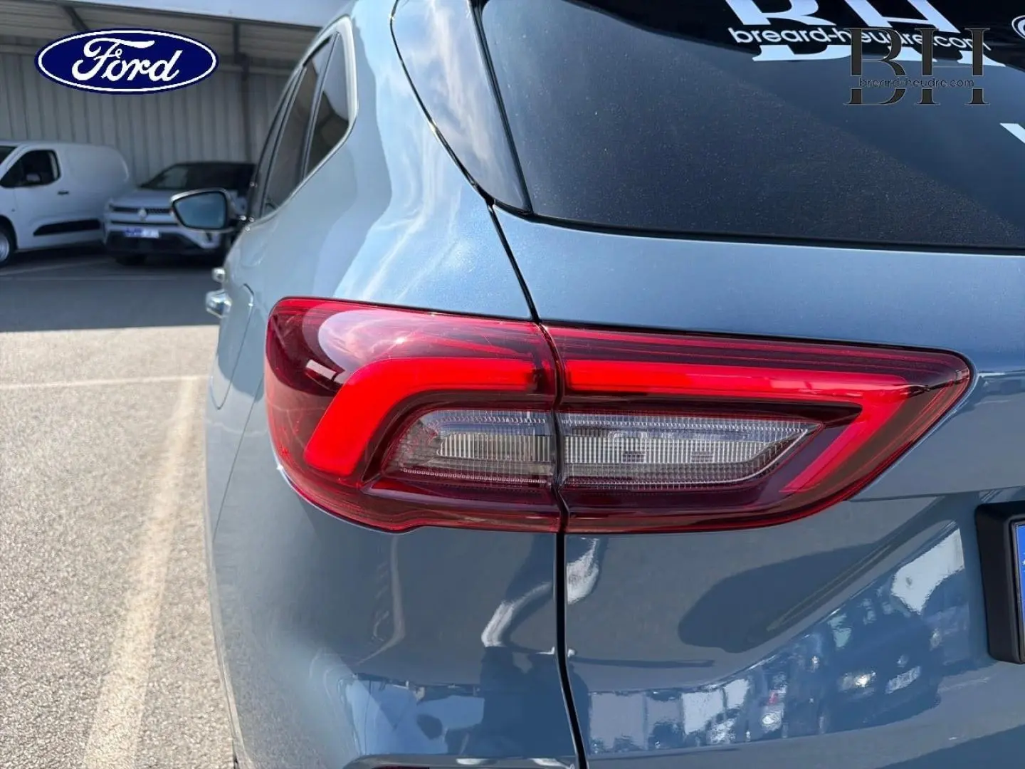 Feu arrière gauche en gros plan du Ford Kuga bleu, vue arrière côté gauche avec reflet sur la carrosserie.