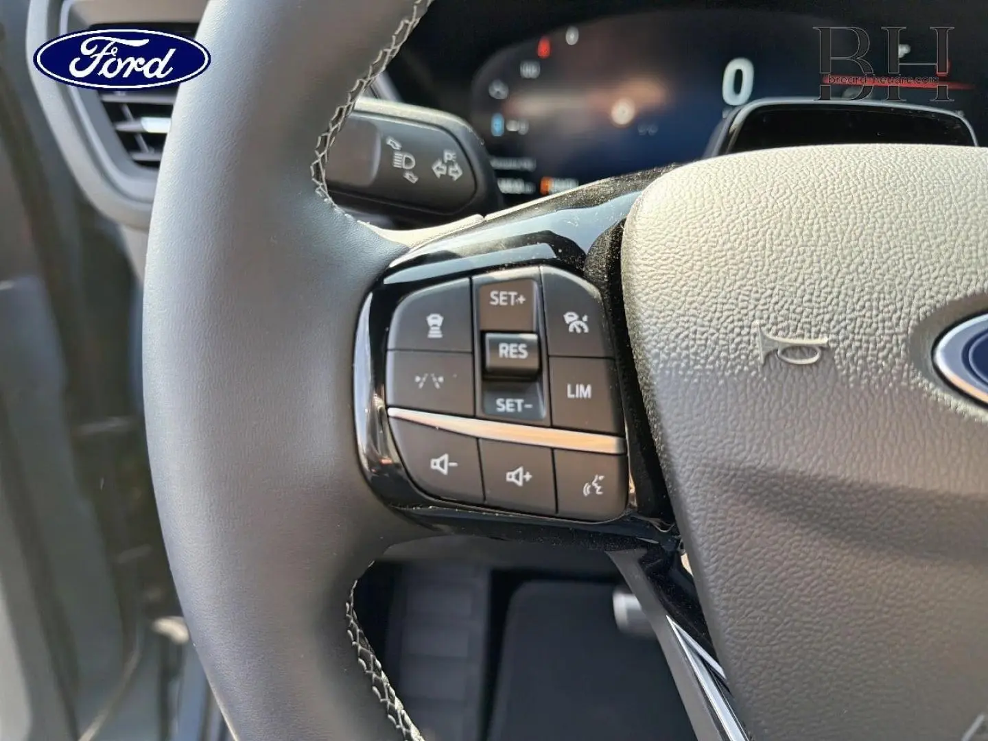 Gros plan sur le volant noir du Ford Kuga 2026 avec commandes multifonctions et logo Ford visible.