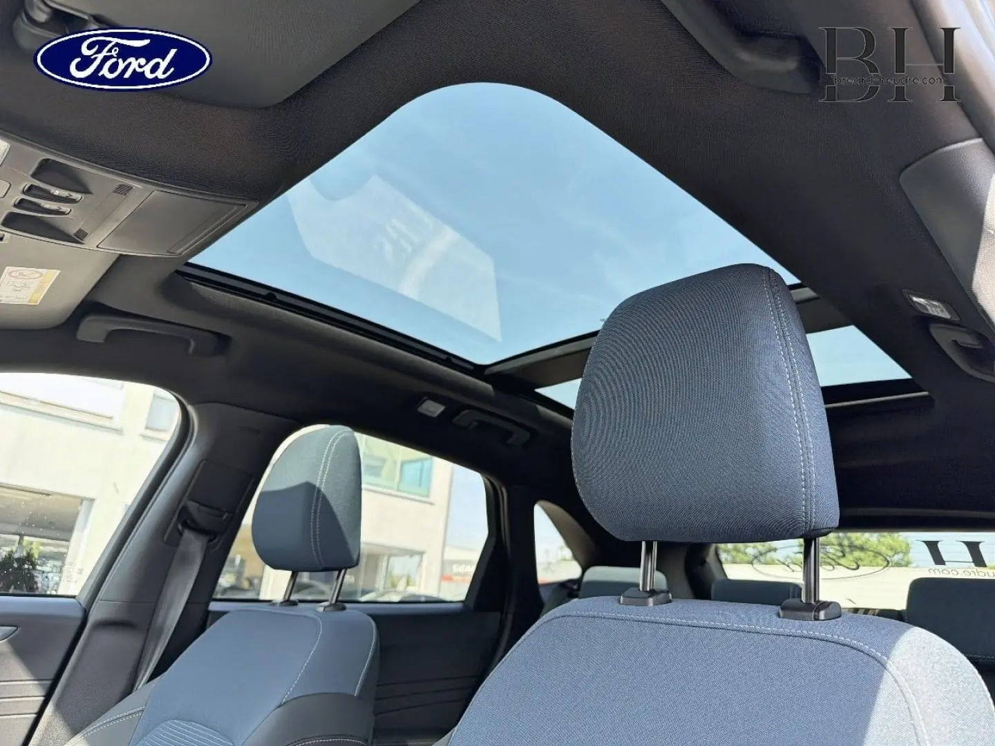 Vue intérieure du Ford Kuga 2026 montrant les sièges avant gris et le toit ouvrant panoramique en verre.
