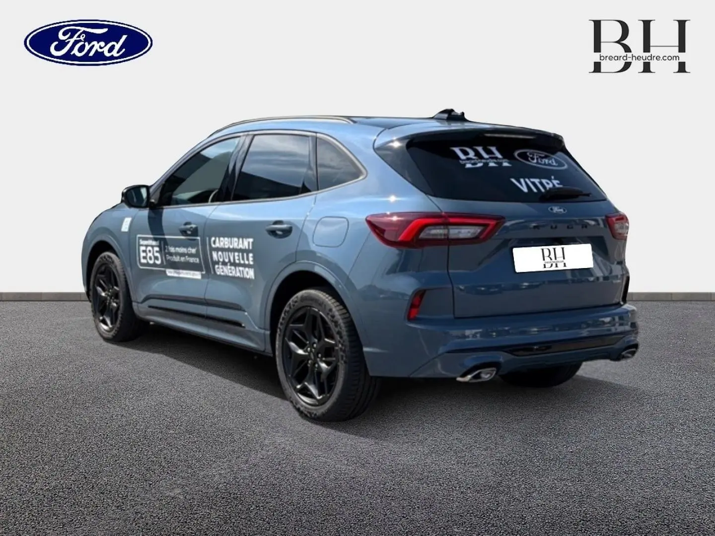 Vue 3/4 arrière droite d'un Ford Kuga bleu métallisé avec jantes noires et marquages publicitaires sur les portes.