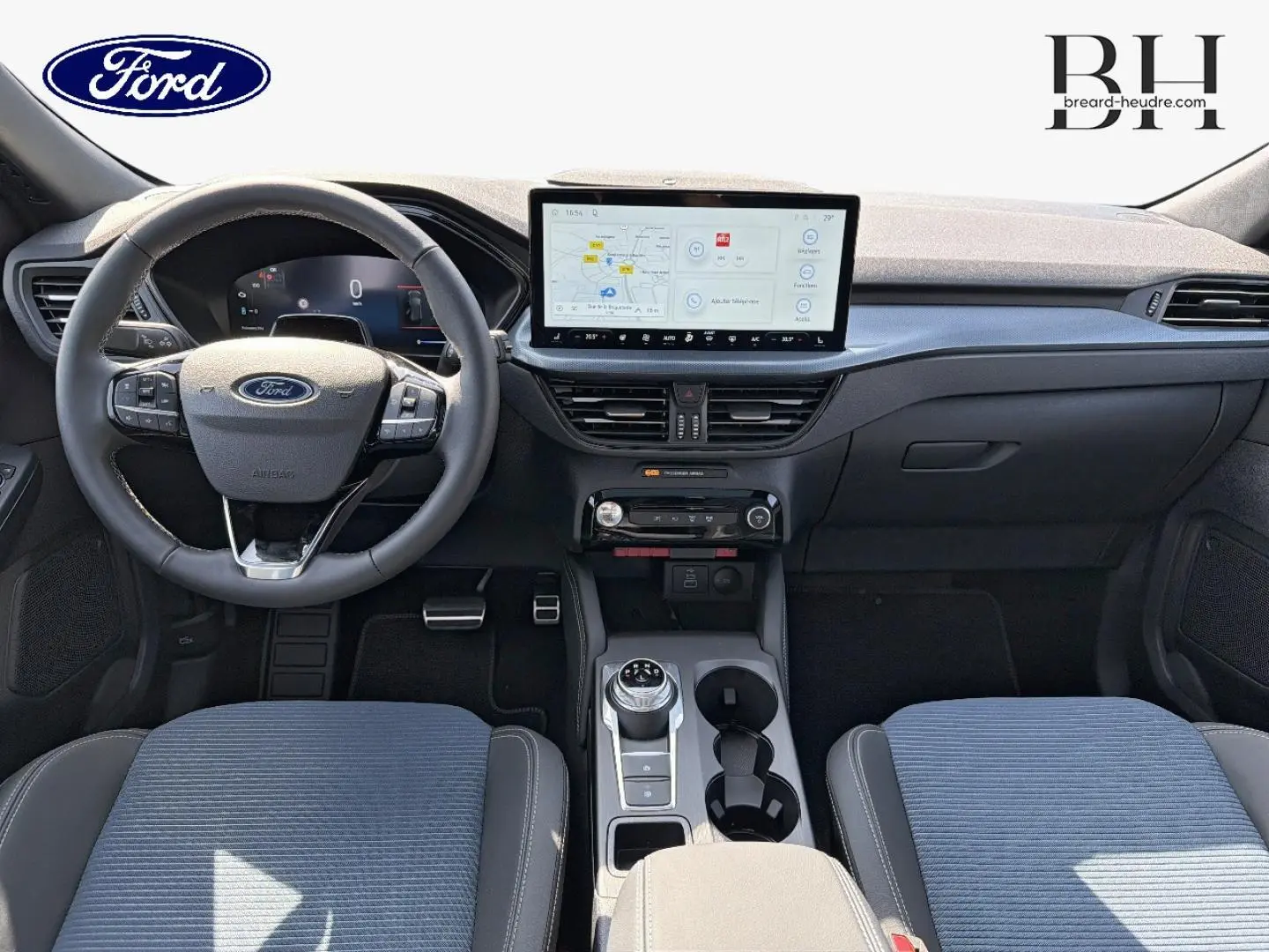 Vue intérieure frontale du Ford Kuga 2026 montrant le volant multifonction, écran tactile central et sièges tissu bleu et cuir noir.
