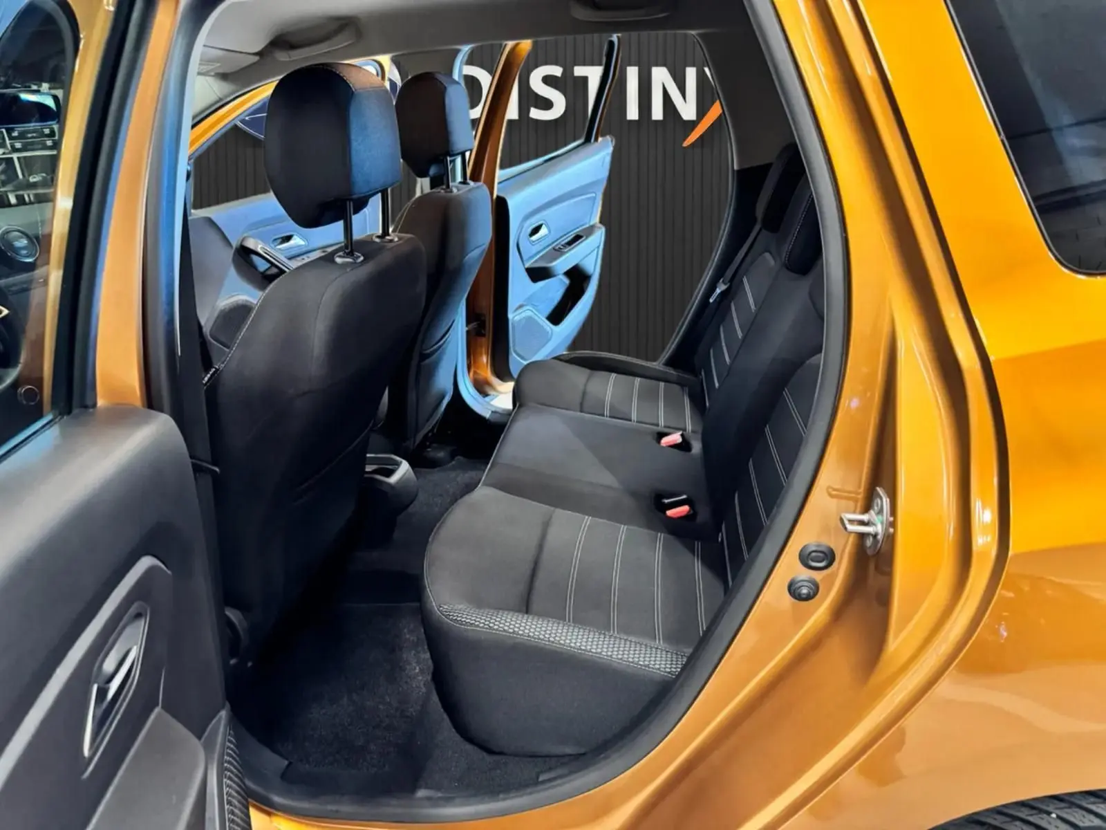 Vue intérieure côté droit arrière du Dacia Duster orange 2020, montrant les sièges arrière noirs et la porte ouverte.