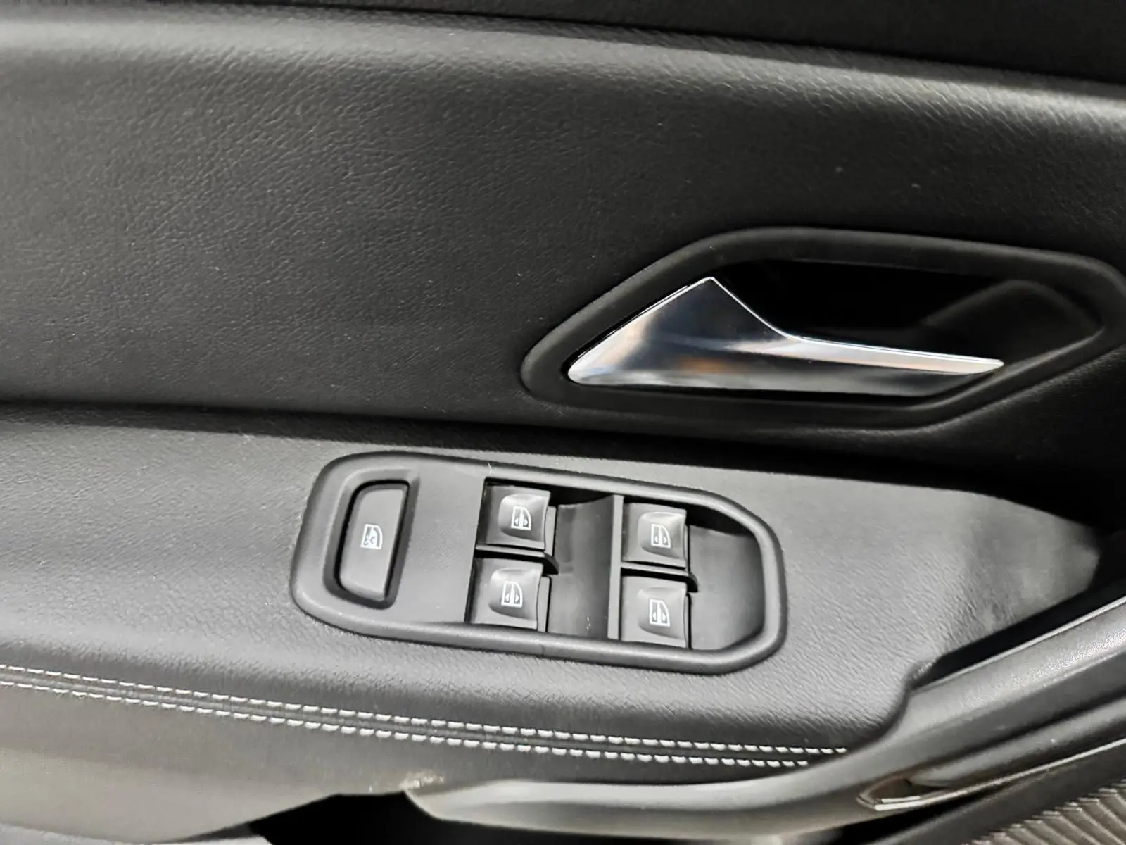 Gros plan sur la commande des vitres électriques et la poignée intérieure en plastique noir du côté gauche du Dacia Duster 2020.
