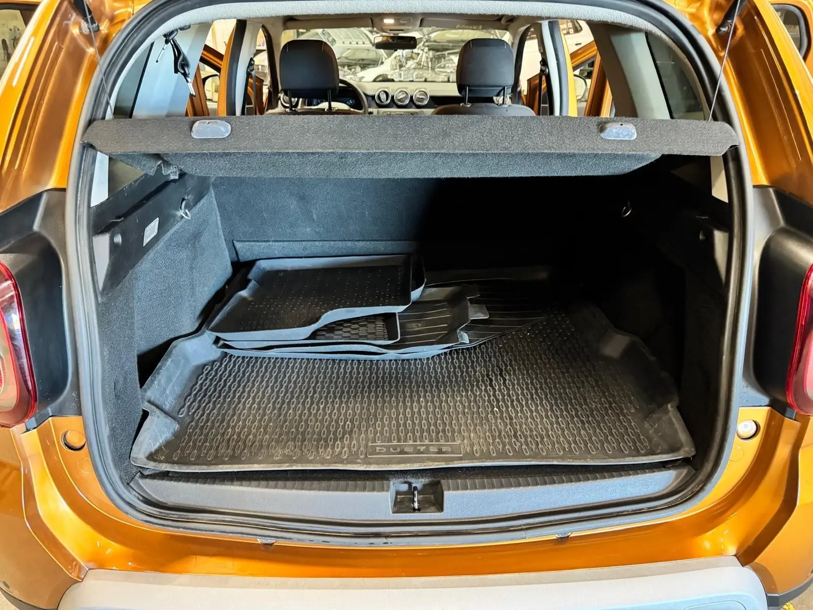 Vue arrière du coffre ouvert d’un Dacia Duster orange 2020 avec tapis de sol en caoutchouc noir.