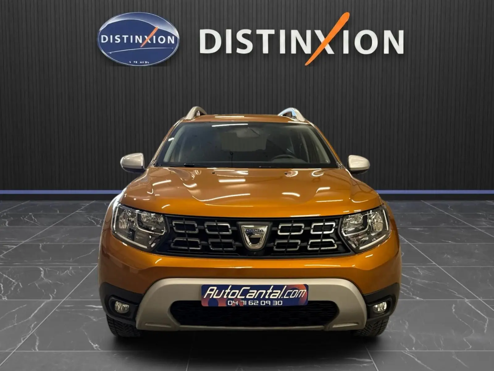Vue frontale d'un Dacia Duster orange 2020 avec calandre noire et logo au centre, dans un showroom Distinxion.
