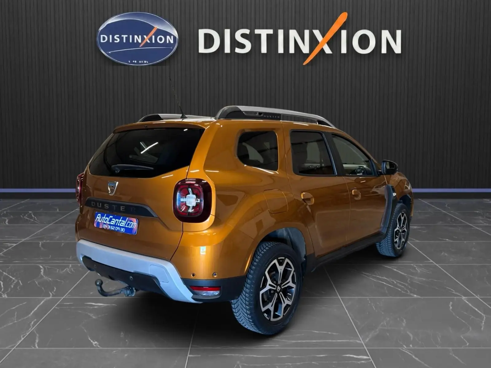 Vue 3/4 arrière droite d'un Dacia Duster orange 2020 avec attelage et jantes bi-ton dans un showroom.