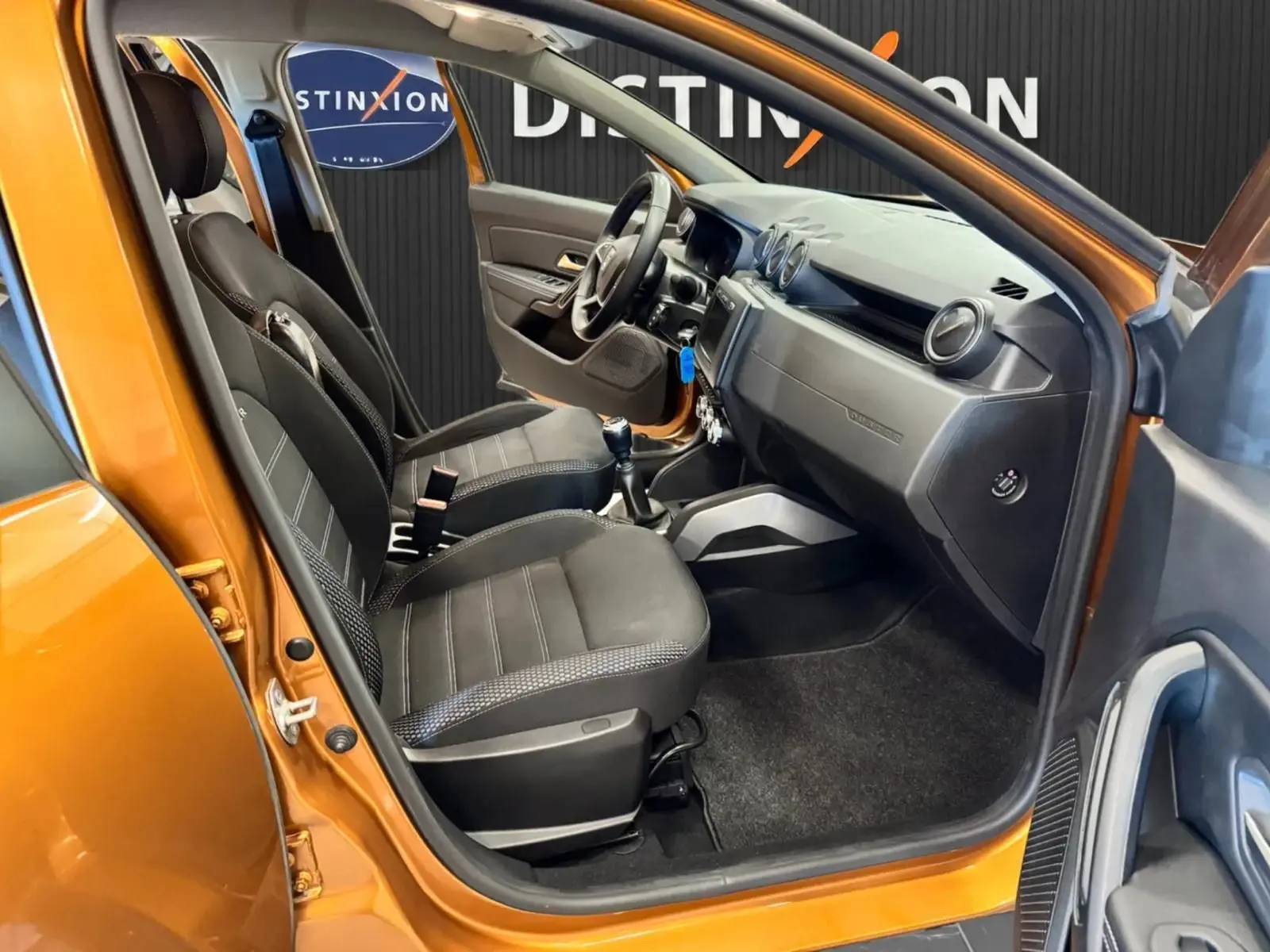Vue intérieure côté conducteur du Dacia Duster orange 2020, sièges noirs et tableau de bord moderne.