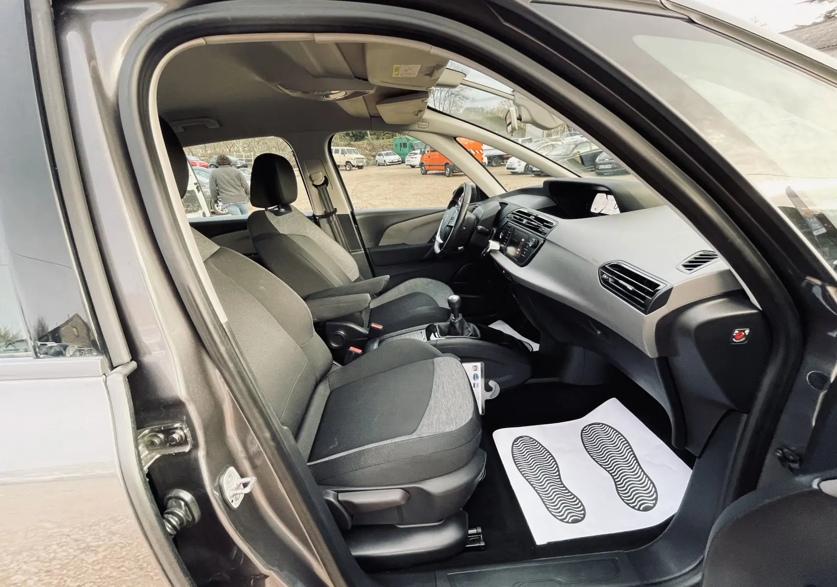 Intérieur de la Citroën C4 Picasso gris, vue côté conducteur ouverte, sièges tissu noir et tableau de bord moderne.