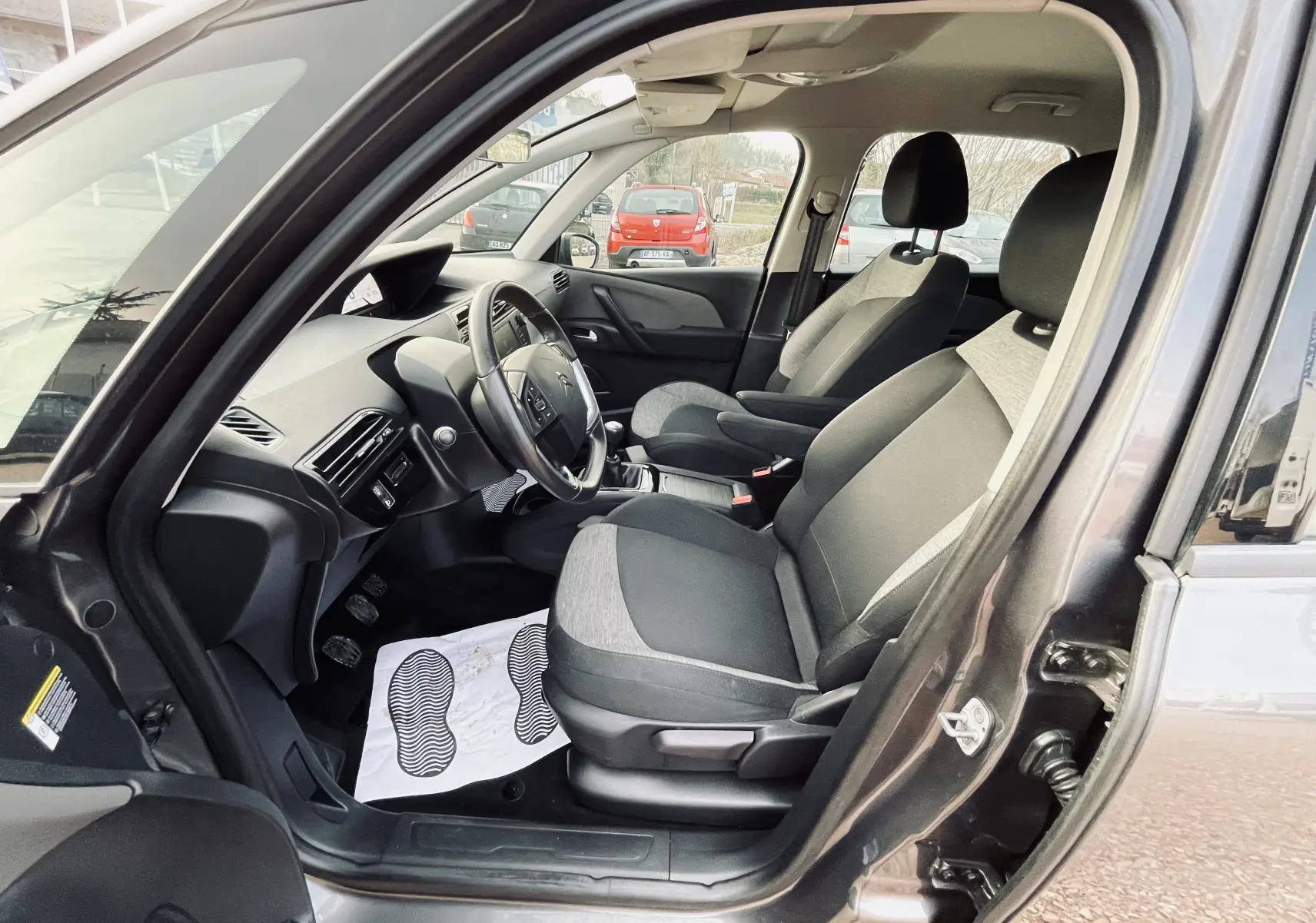 Vue intérieure côté conducteur du Citroën C4 Picasso gris, montrant les sièges tissu noir et gris et le tableau de bord.