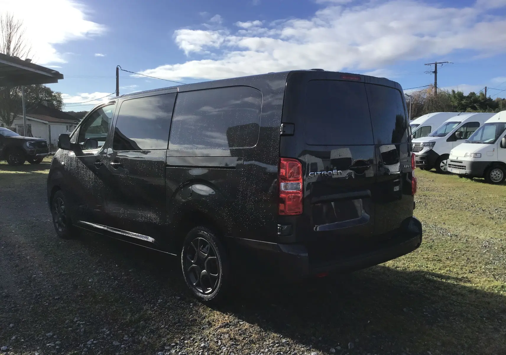 Vue 3/4 arrière droite d'un Citroën Jumpy XL gris titane avec vitres teintées et jantes noires sur un parking extérieur.