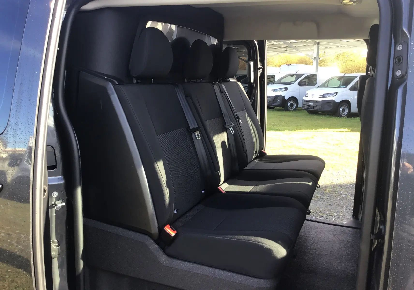 Vue latérale intérieure sur la banquette arrière noire du Citroën Jumpy Cabine Approfondie gris titane avec porte coulissante ouverte.